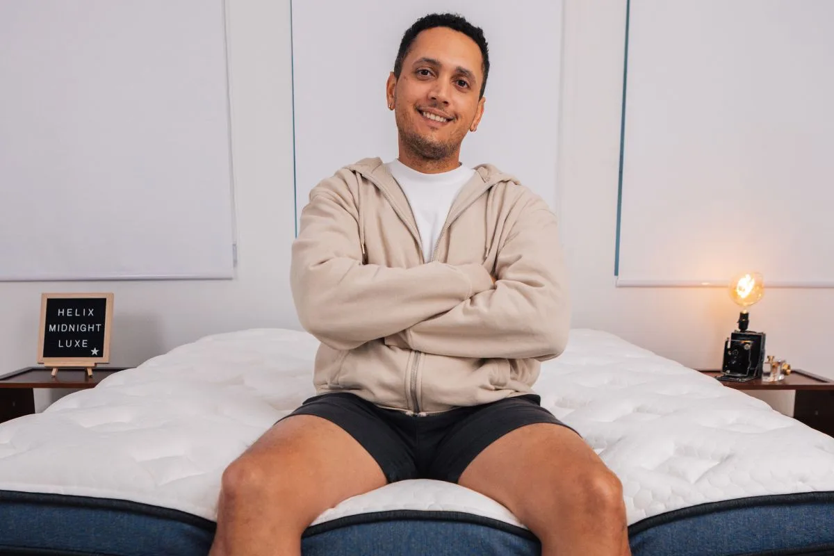 A man in comfortable clothes sitting on the edge of a bed.