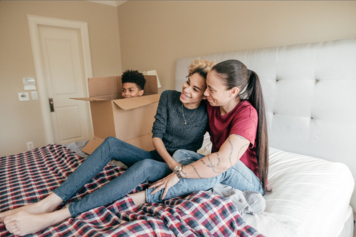 How to Get Rid of a King Size Mattress? family sitting on a bed with a child playing in a cardboard box during a home move.