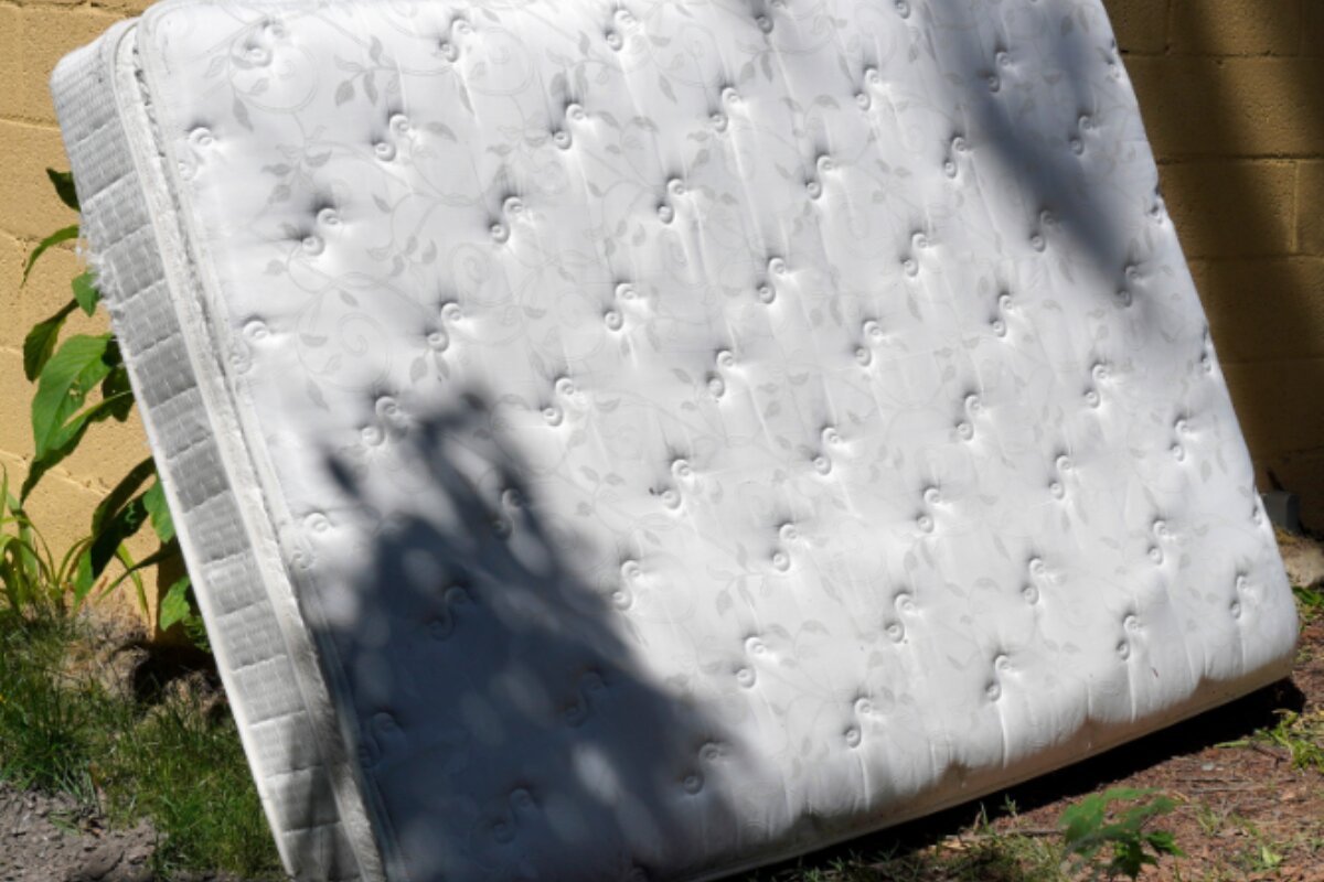 How to Get Rid of a King Size Mattress? old king-size mattress leaning against an outdoor wall for disposal.