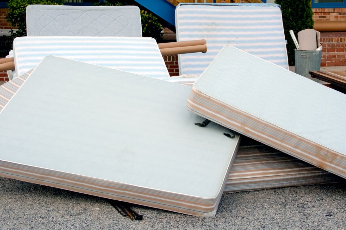pile of old mattresses stacked outside on the curb for disposal or donation.