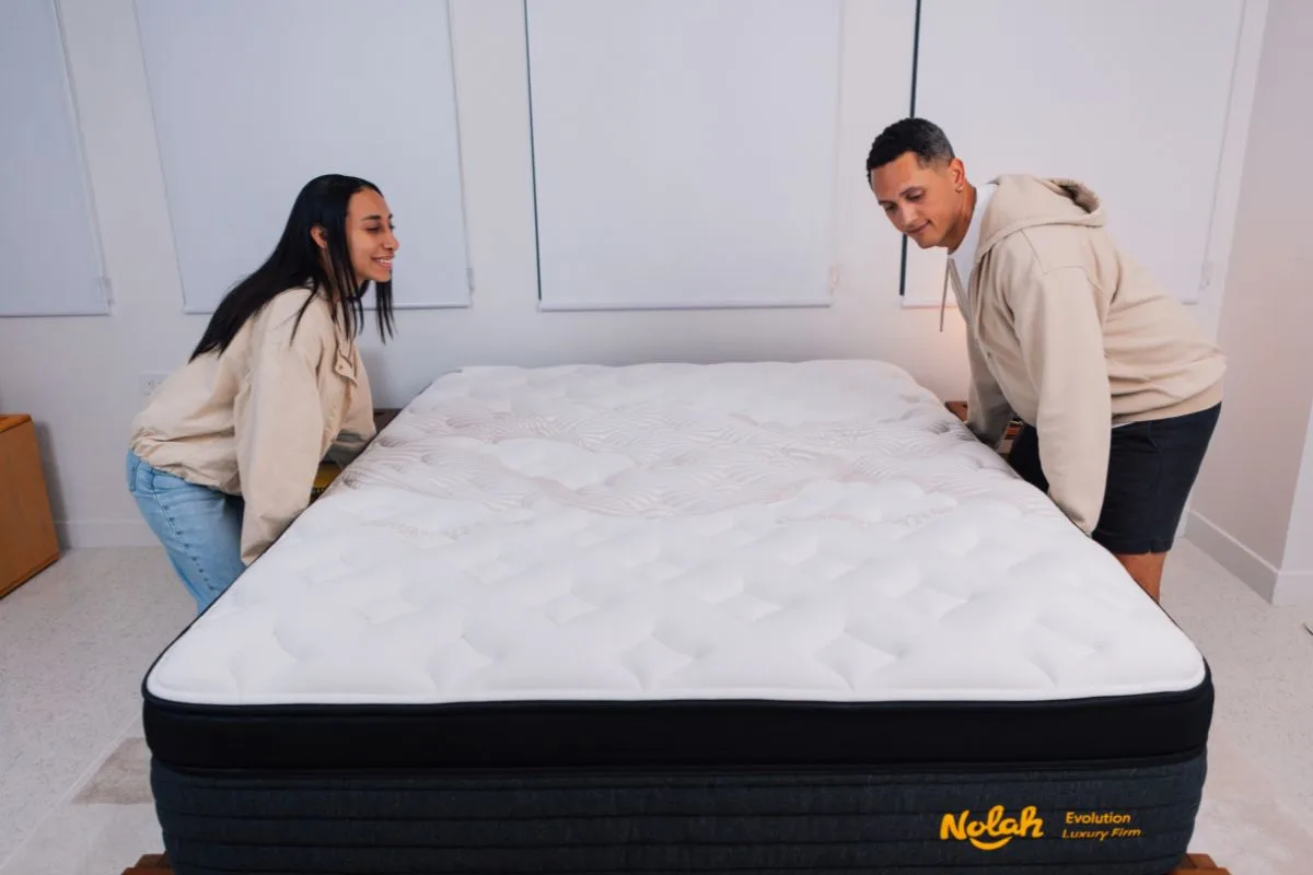 A woman and a man carrying a mattress.