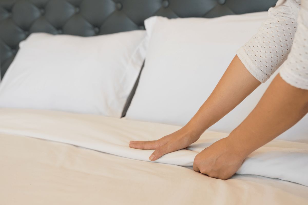 What Is a King Size Bed? Person smoothing sheets on a king size bed showing surface area and bedding setup