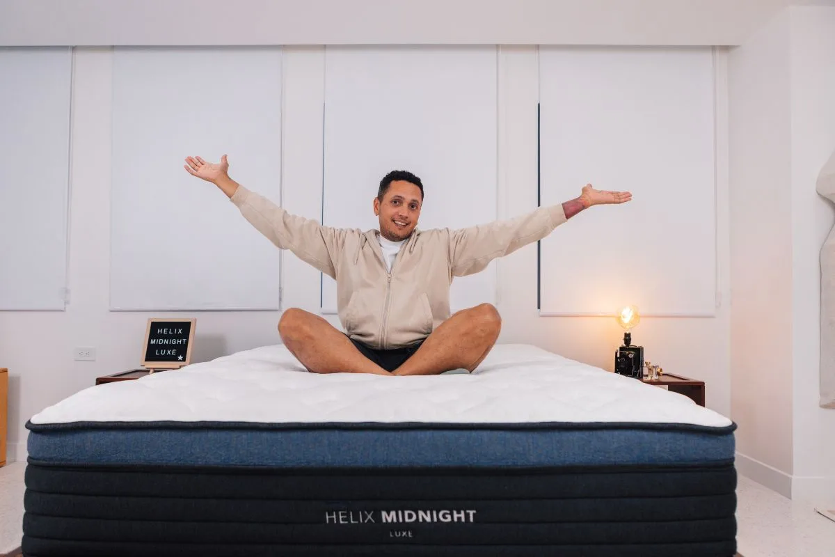 A man in comfortable clothes with his arms out sitting on the Helix Midnight Luxe.