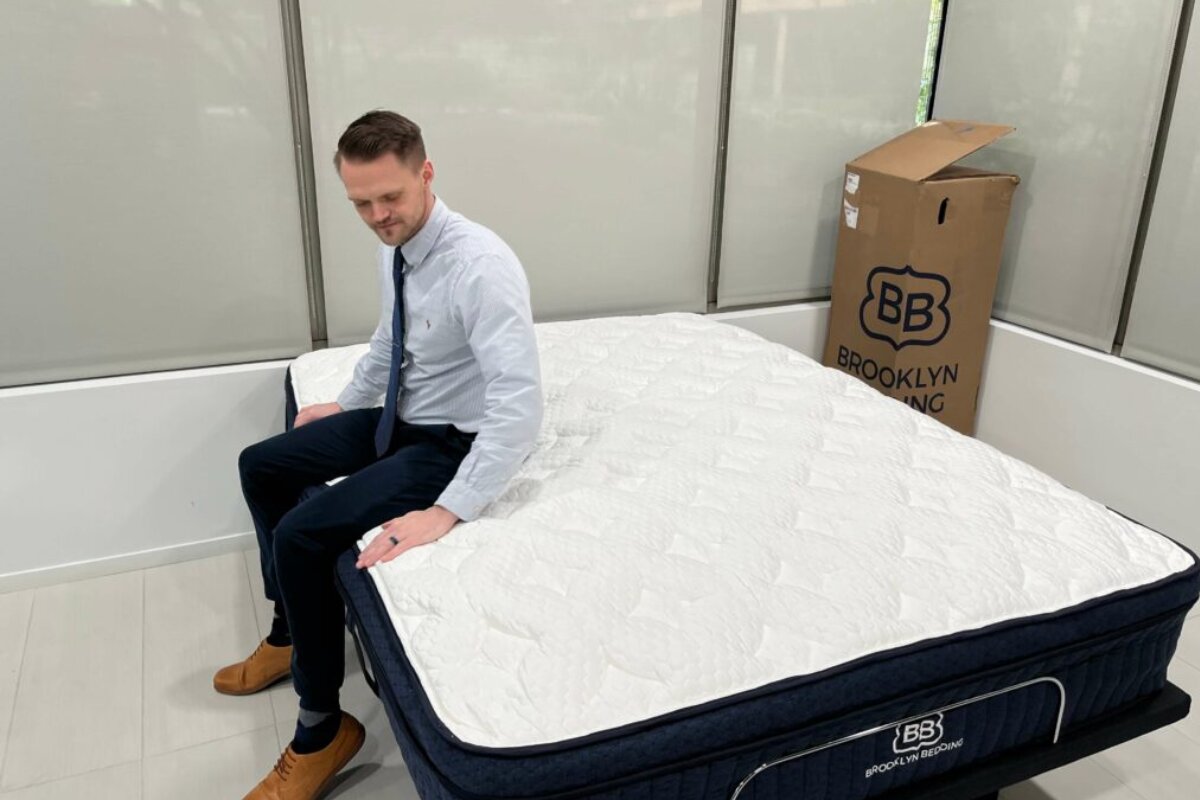 person sitting on Brooklyn Bedding Aurora Luxe Cooling mattress with shipping box in background