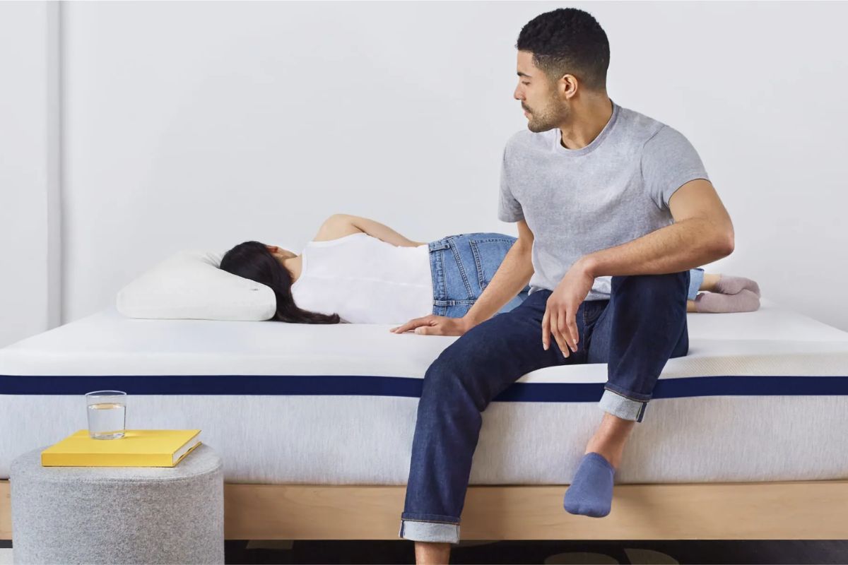 A woman lying down on a hybrid bed while the man sits on the edge.