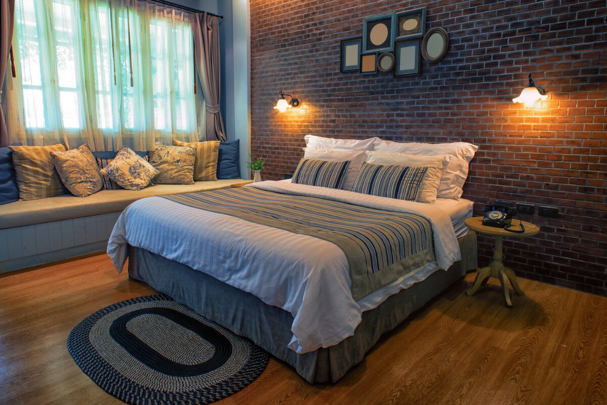 cozy bedroom with brick accent wall, wooden floor, and neatly made bed with striped pillows