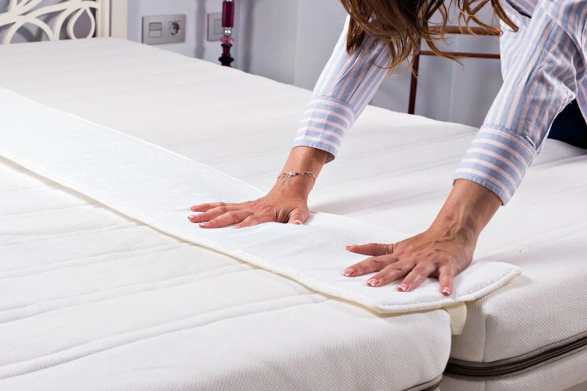 person placing mattress gap filler between split king mattresses to create a seamless surface