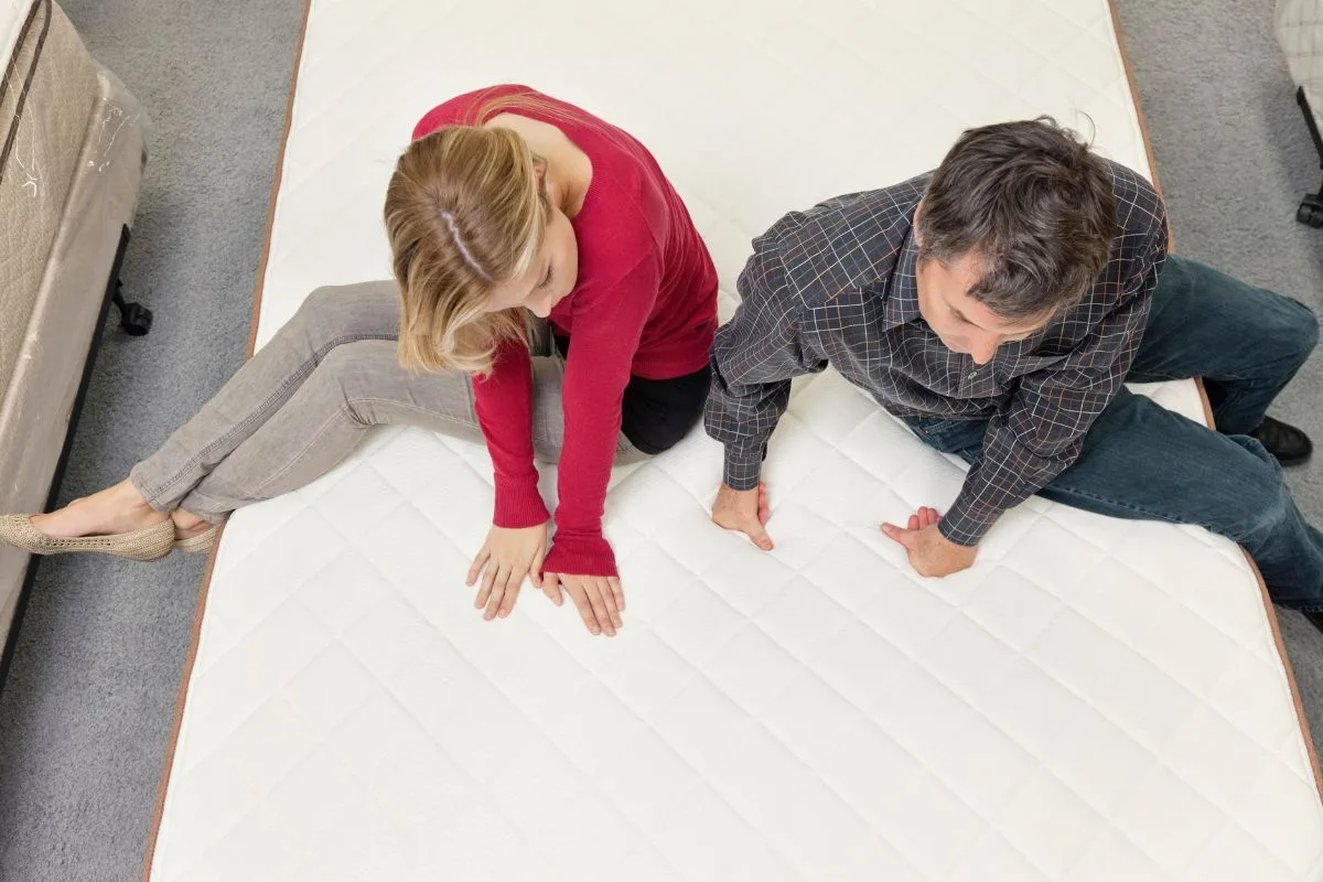 How Much is a California King Mattress? Couple sitting on a mattress in showroom evaluating comfort and value of a California King mattress