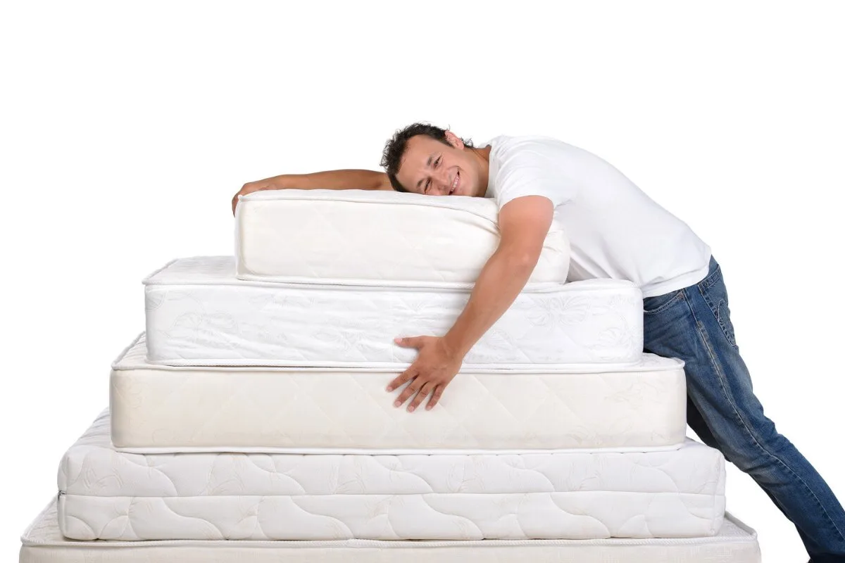 How Much Does a King Size Mattress Weigh? man hugging stacked mattresses of different sizes, showing comfort and mattress thickness comparison