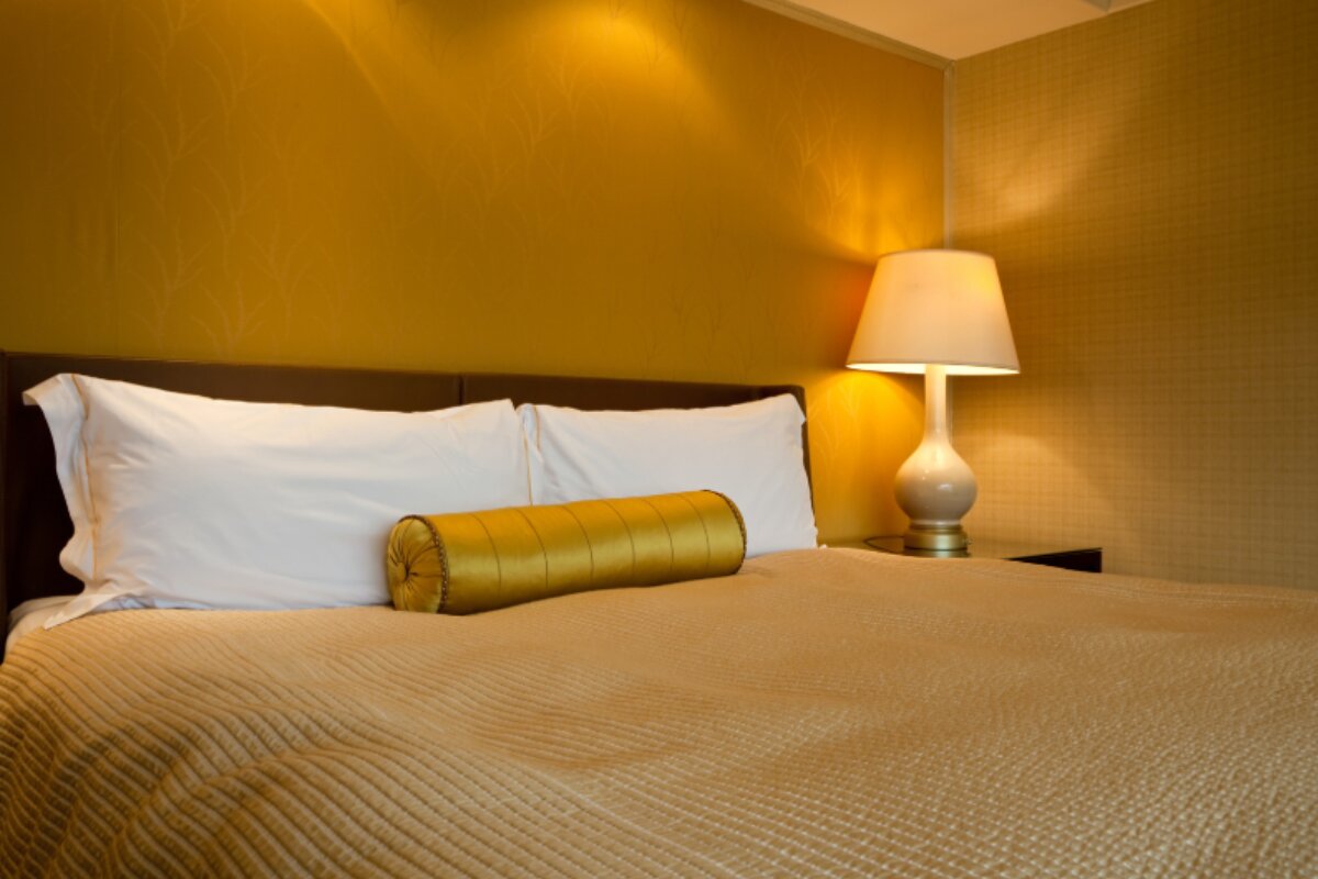 warm bedroom with yellow lighting, neatly made bed, and bedside lamp creating a cozy atmosphere