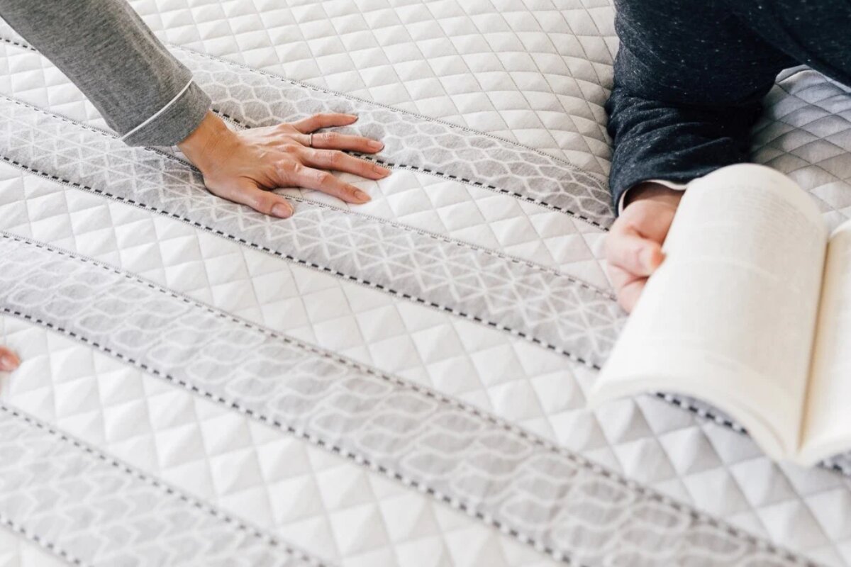 hand pressing the surface of a Leesa Sapira Hybrid mattress while a person reads on it