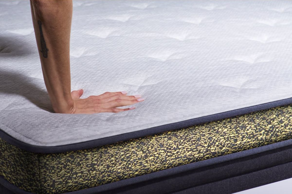 A person pressing on a hybrid mattress.