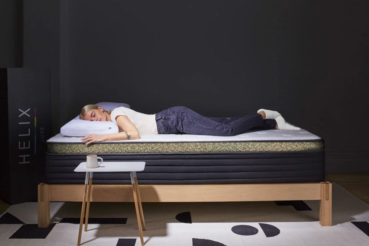 A person laying down on a hybrid mattress with the Helix delivery box next to them.