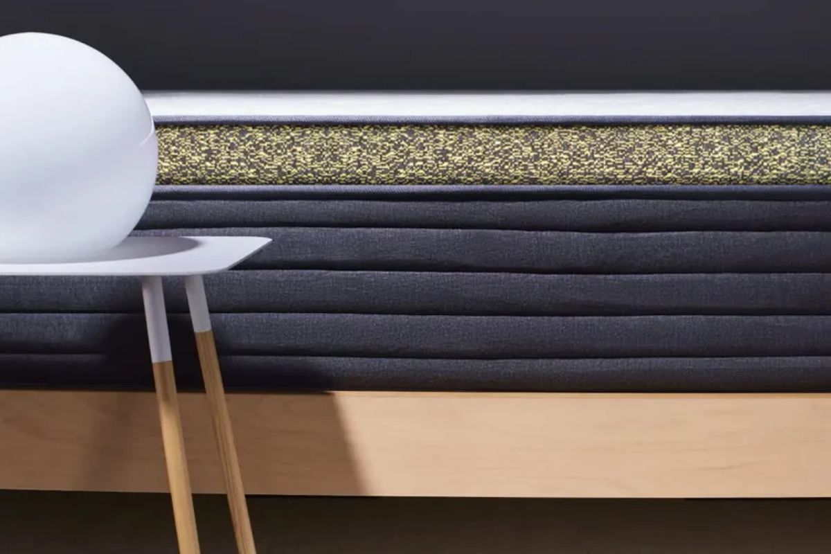 A close up of a hybrid mattress with a sidetable and a lamp sitting on it.