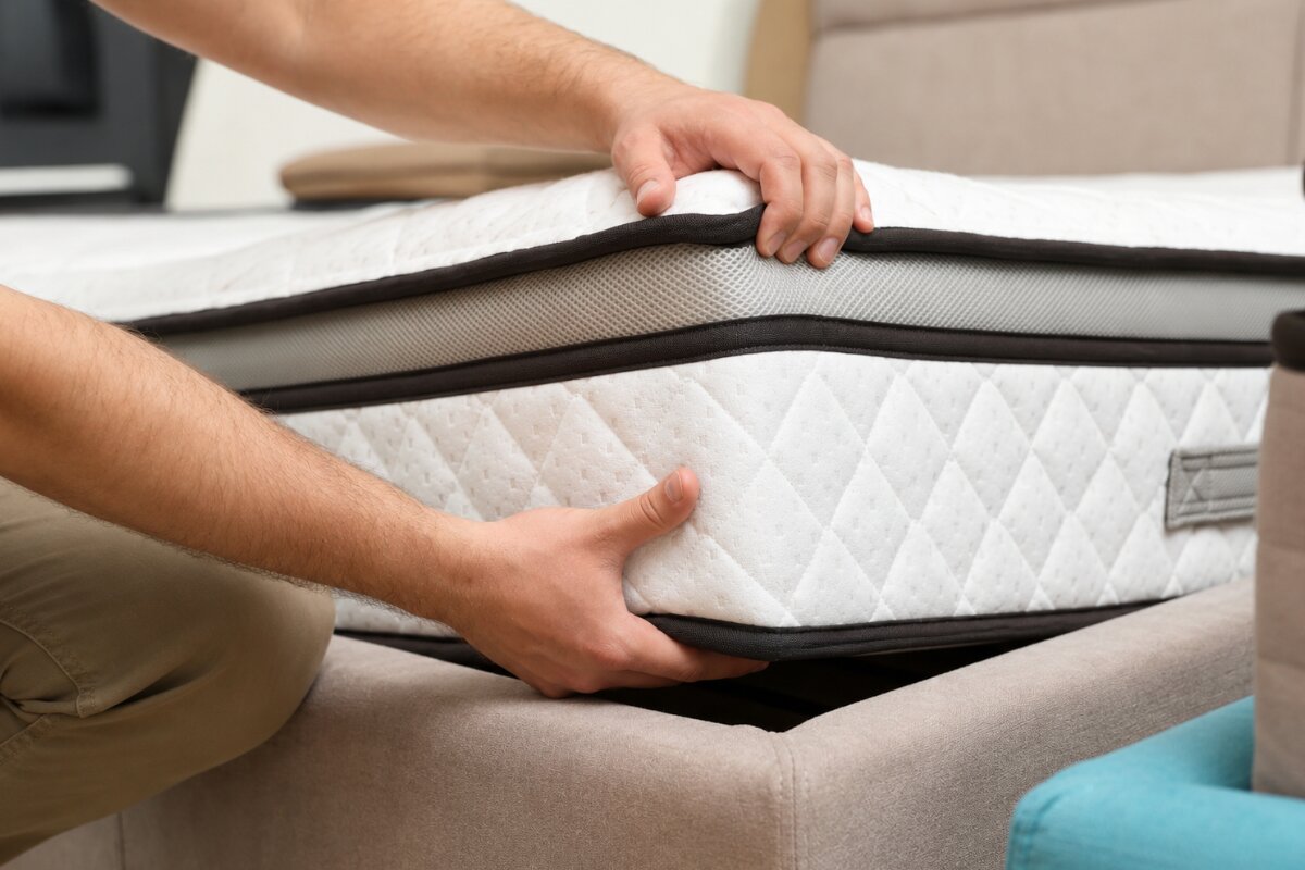 How Big is a Full XL Mattress? person lifting and positioning full xl mattress onto upholstered bed frame during bedroom setup
