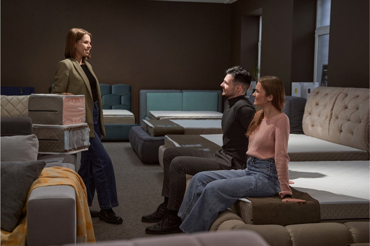 How Much Is a Queen Size Mattress? couple shopping for a queen size mattress with a salesperson in a mattress showroom