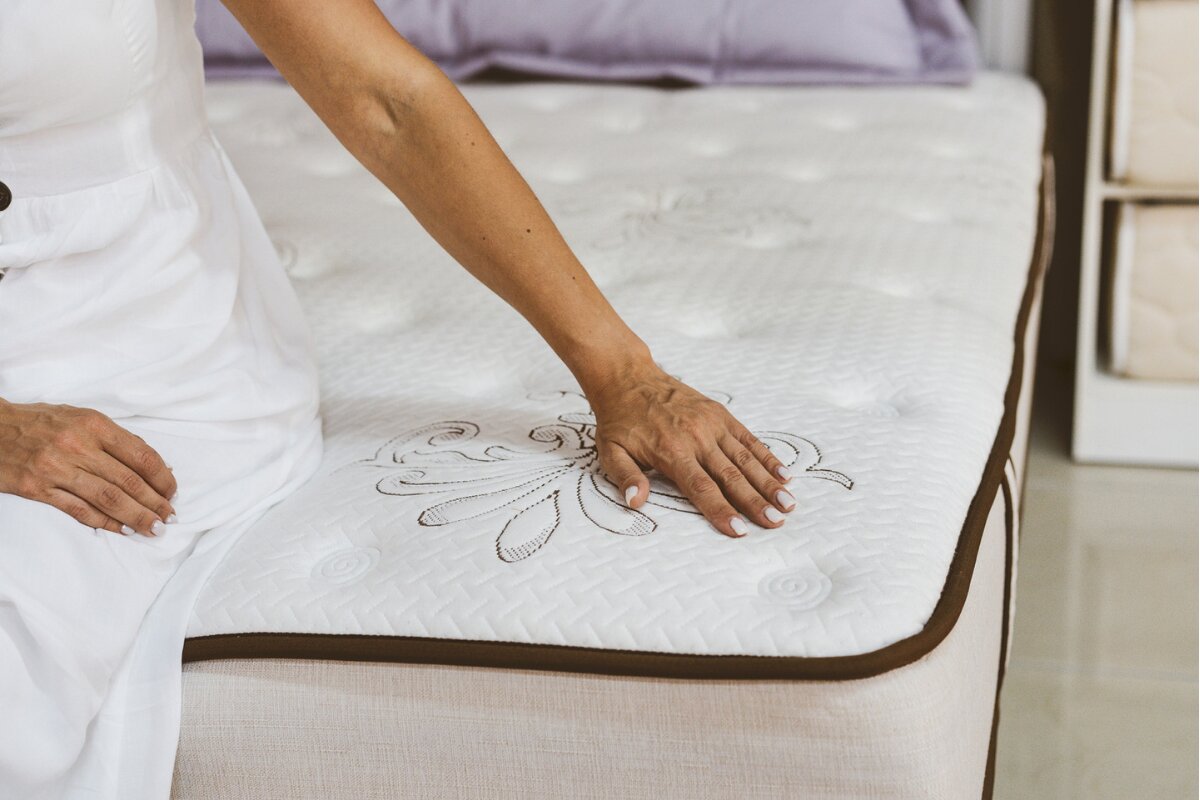 How Much Is a Queen Size Mattress? person pressing on a queen size mattress surface to test comfort and support