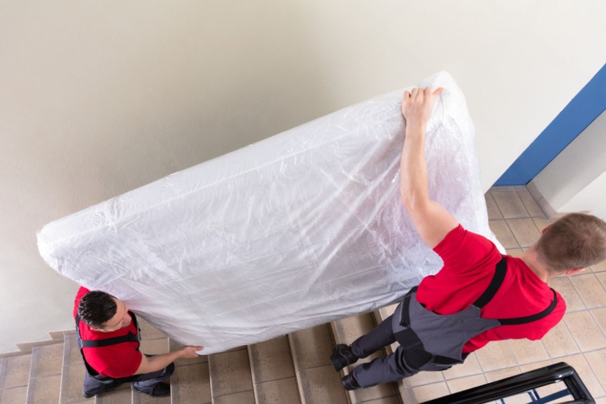 How to Transport a Full Size Mattress Like a Pro? Movers carefully carrying a full size mattress down stairs with protective plastic wrap