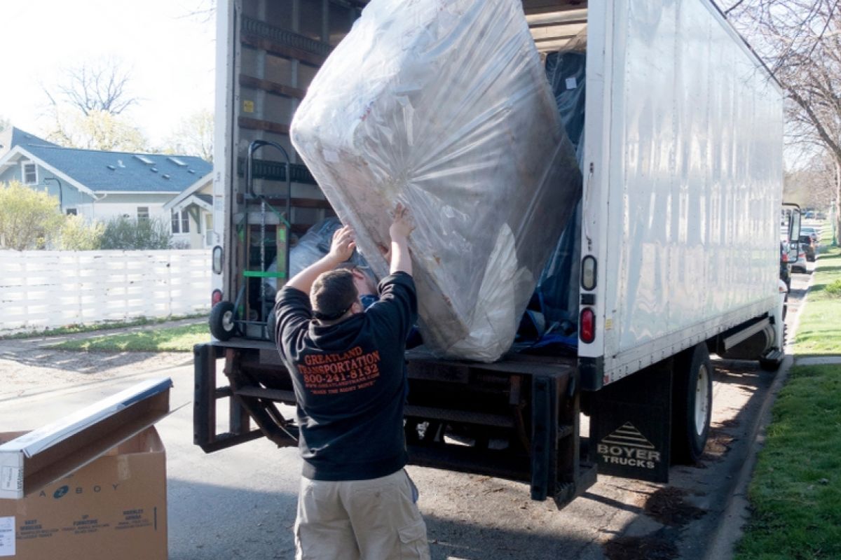 How to Transport a Full Size Mattress Like a Pro? Person lifting a plastic-wrapped full size mattress into a moving truck for relocation