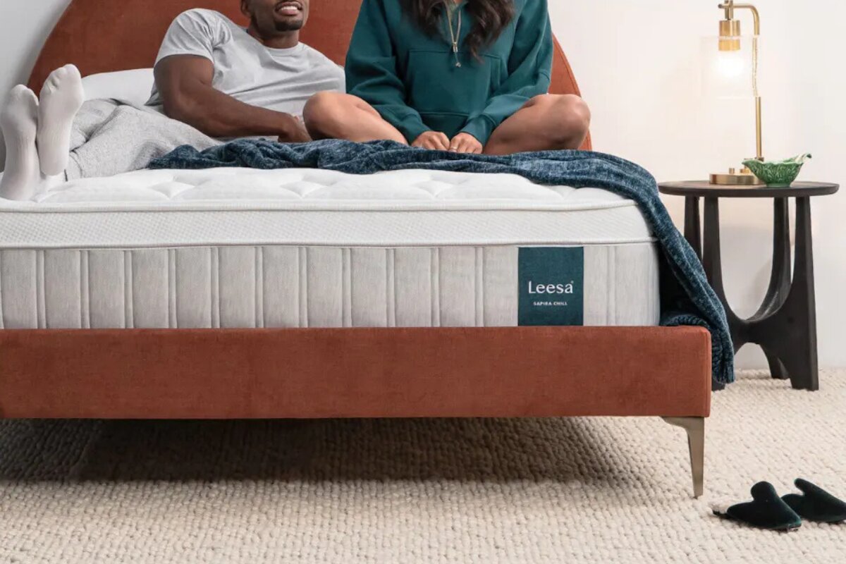 What to Expect When Returning a Leesa Sapira Chill Hybrid Mattress couple relaxing on the leesa sapira chill hybrid mattress with a blue blanket on a brown upholstered bed frame
