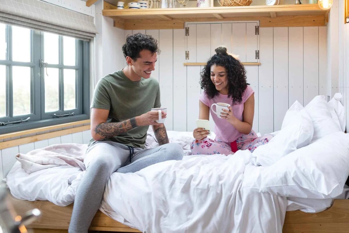 couple relaxing on bed with coffee and phone in cozy bedroom cabin