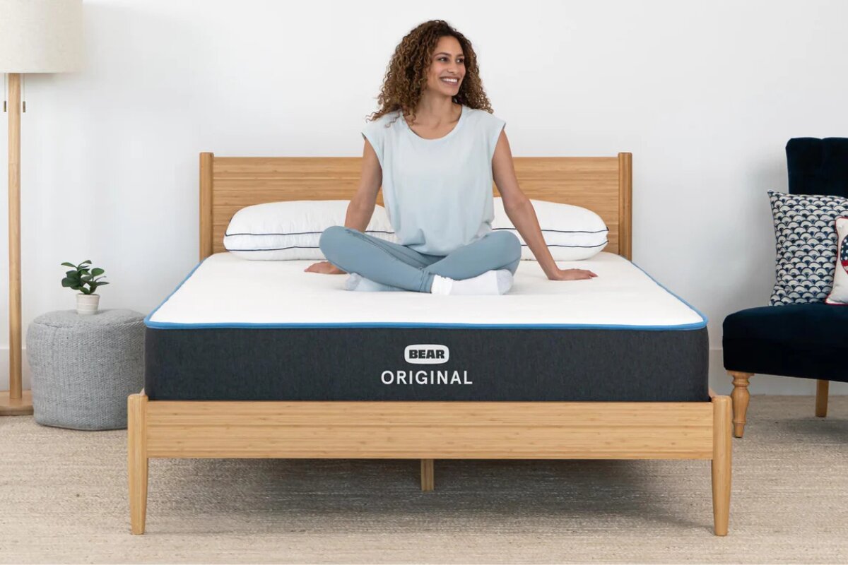 woman sitting cross legged on bear original mattress in a bright bedroom