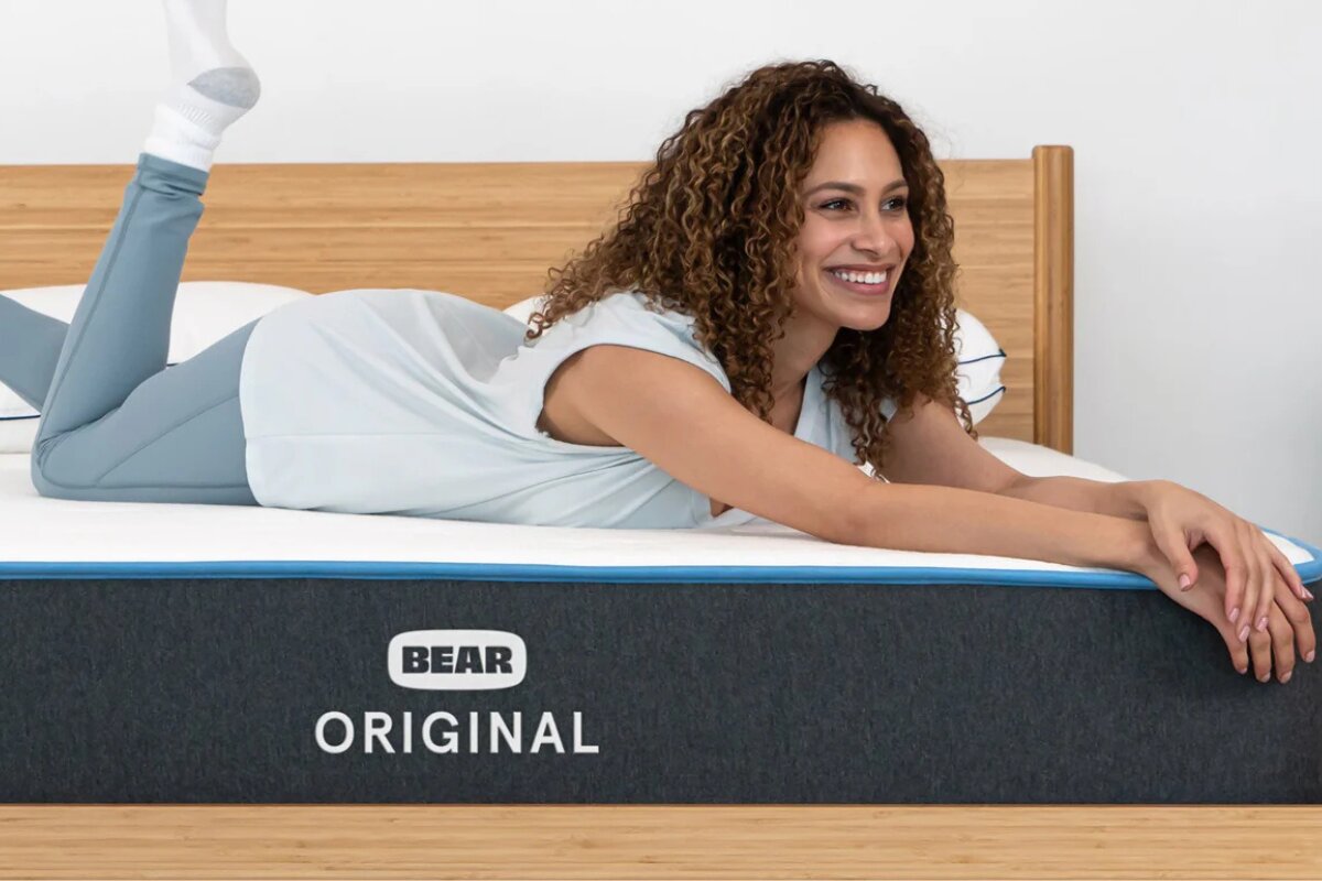 woman lying on bear original mattress smiling with arms stretched out on bed
