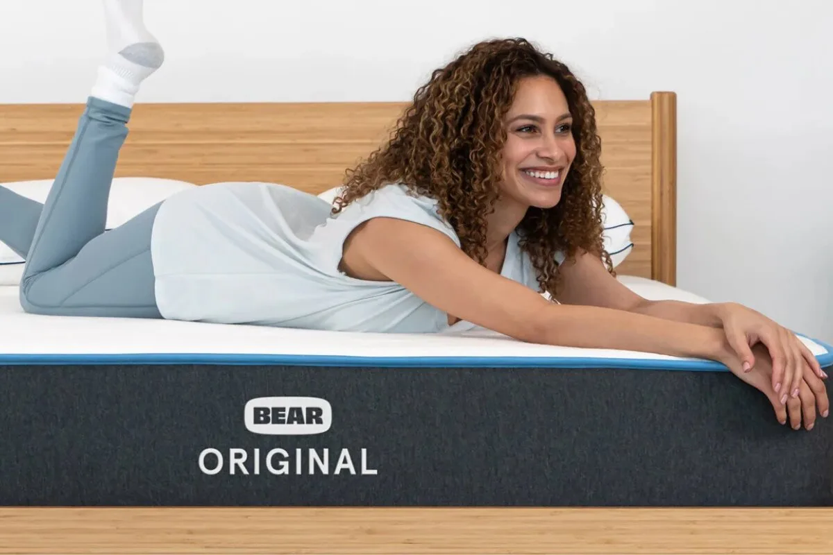 woman lying on bear original mattress smiling with arms stretched out on bed