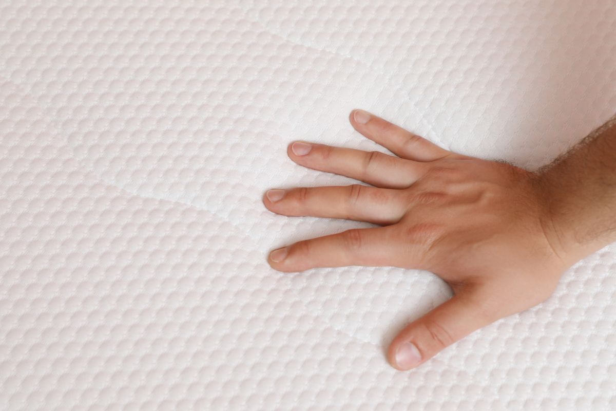 Hand pressing into memory foam mattress surface to test firmness and support level
