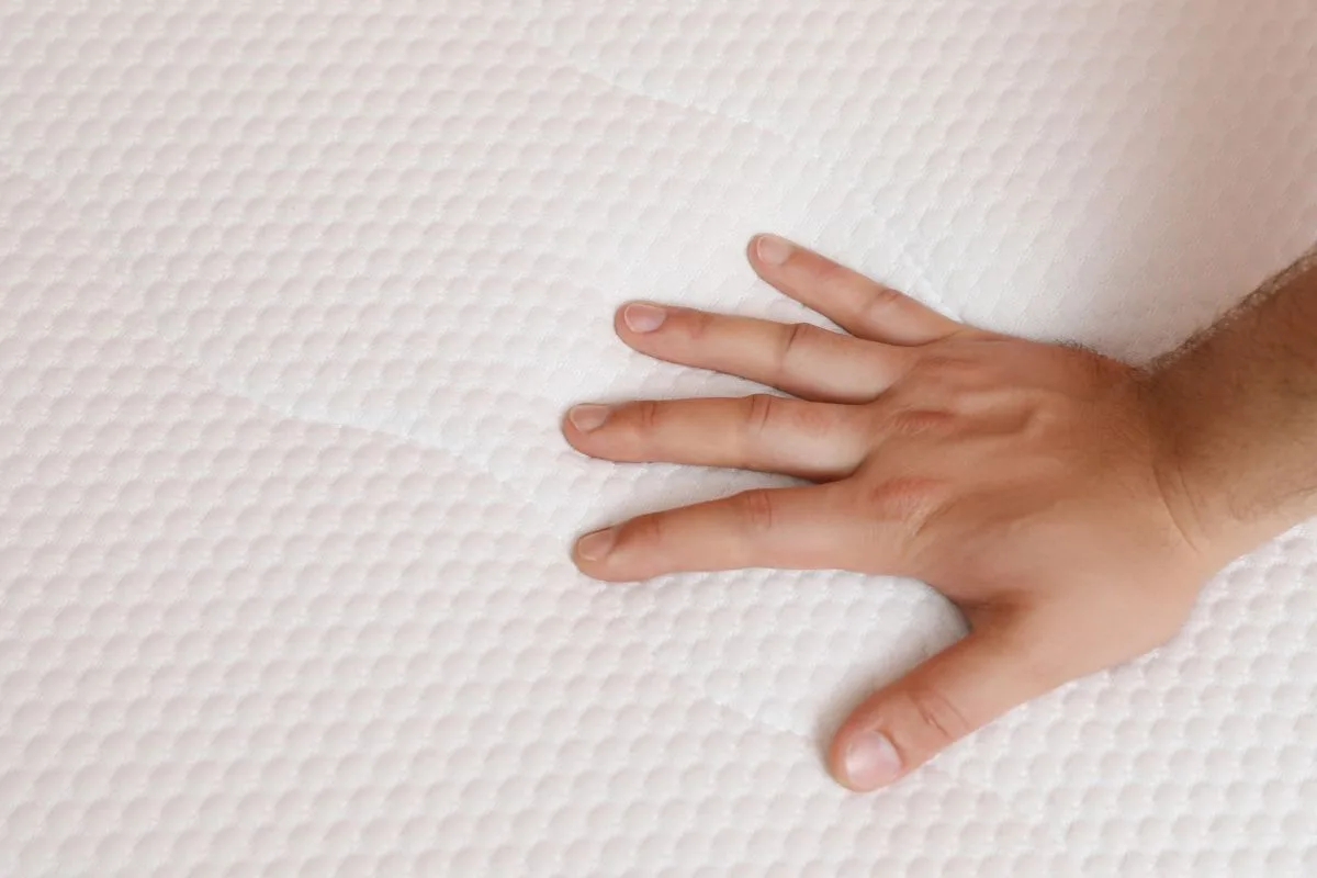 Hand pressing into memory foam mattress surface to test firmness and support level