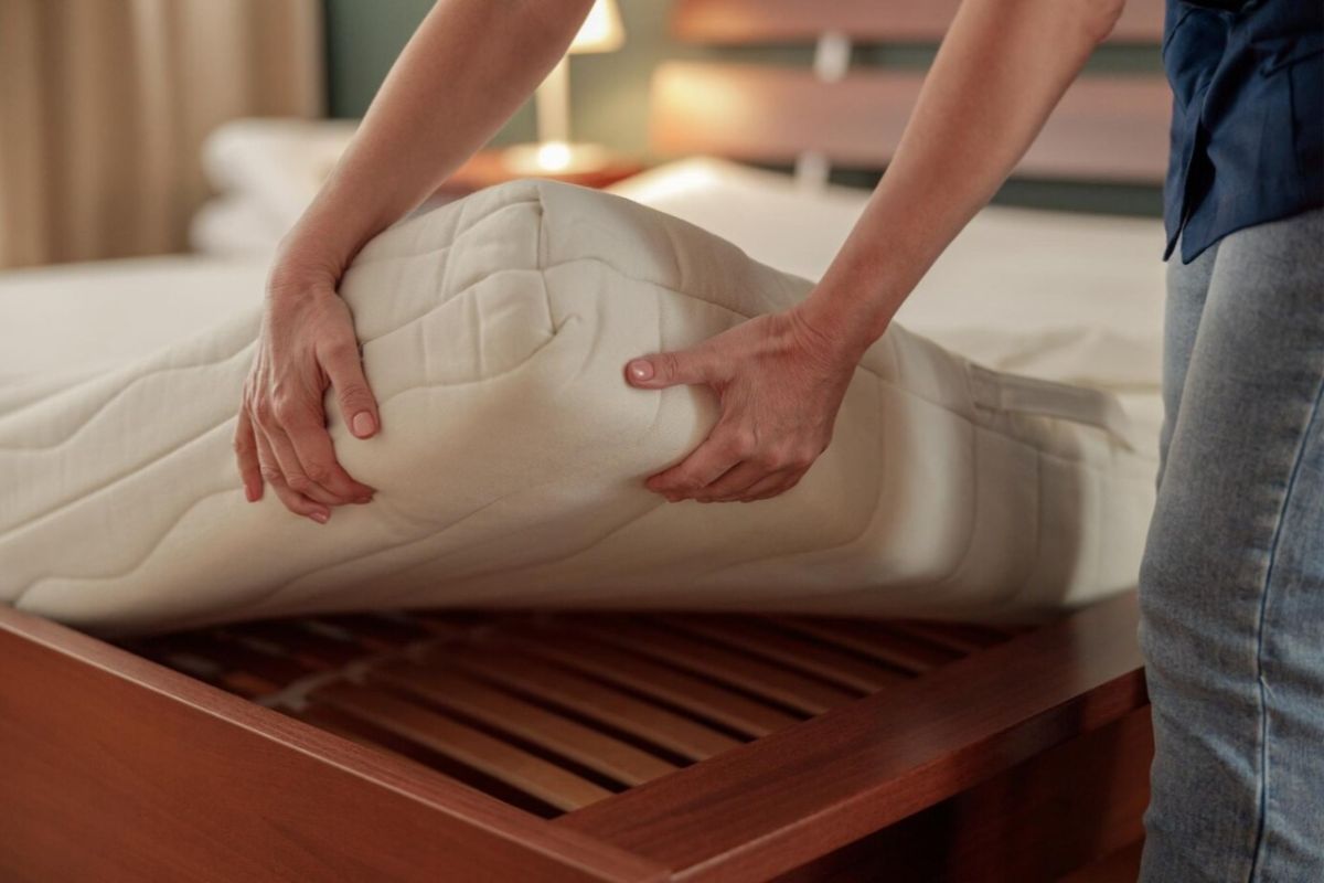Person adjusting a mattress topper on a bed frame to improve mattress firmness and reduce excessive sinkage