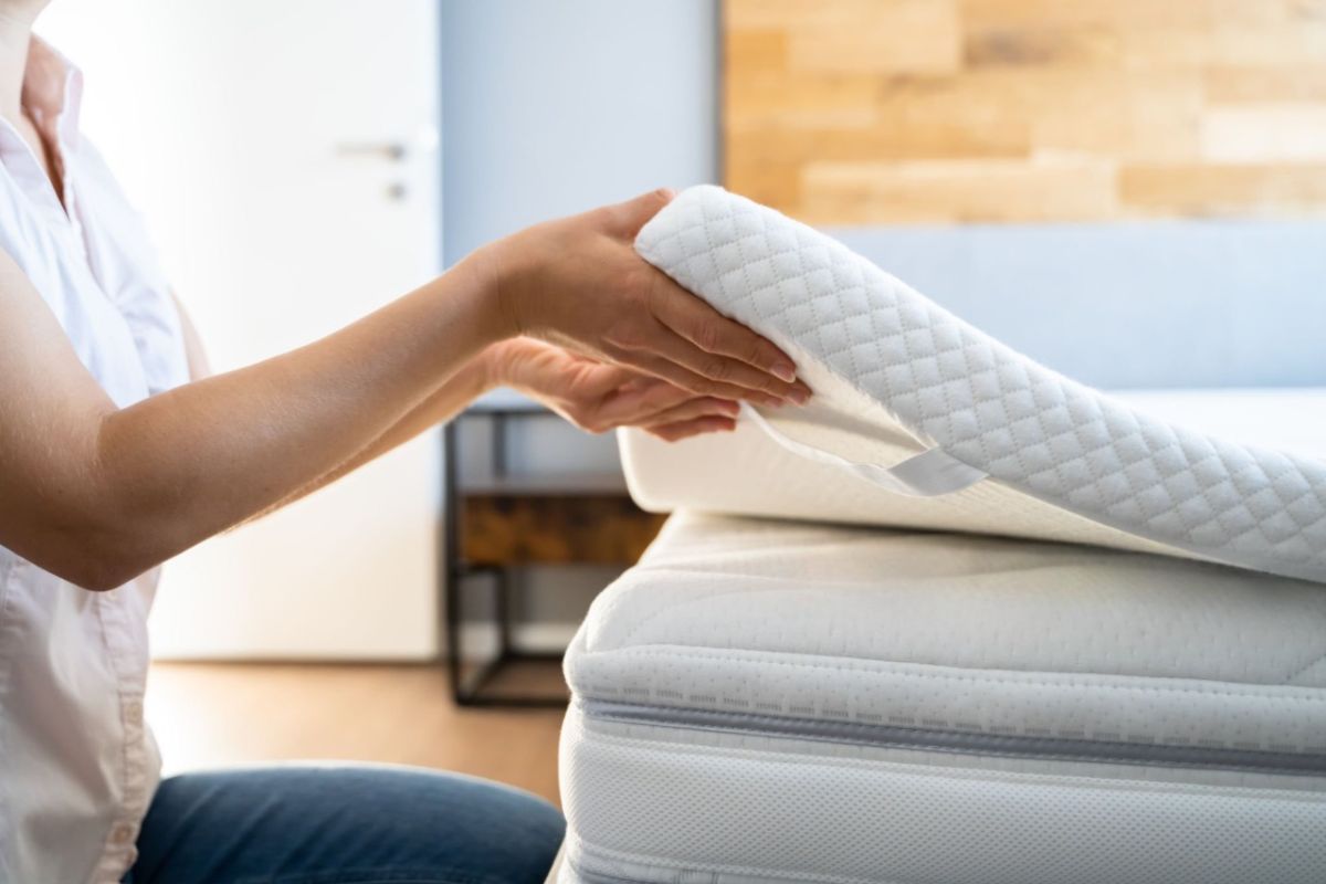Sleeper placing a firm mattress topper on a soft mattress to improve support and reduce sinkage