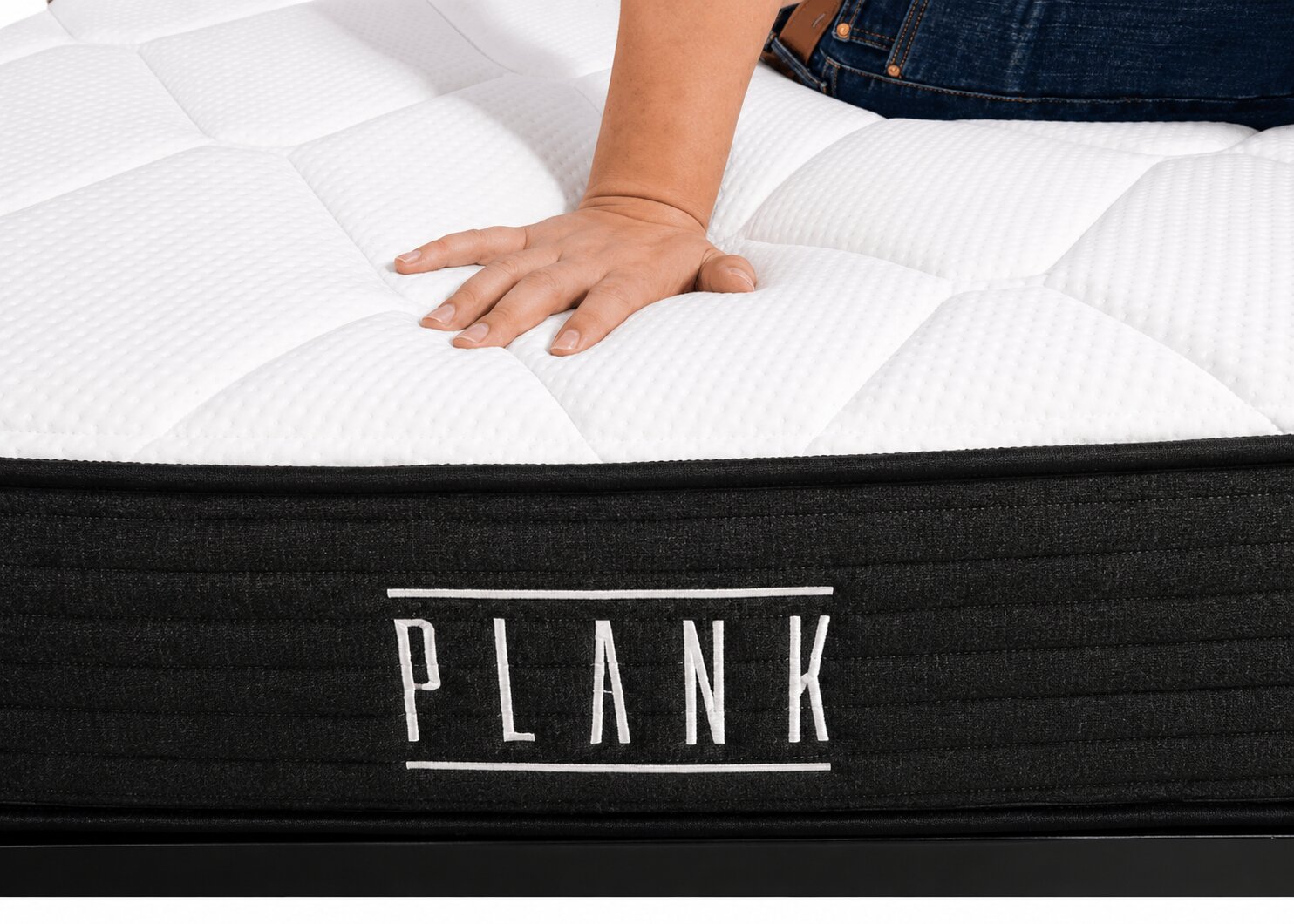 close-up of a hand pressing into the surface of a plank mattress to show firmness and cushioning