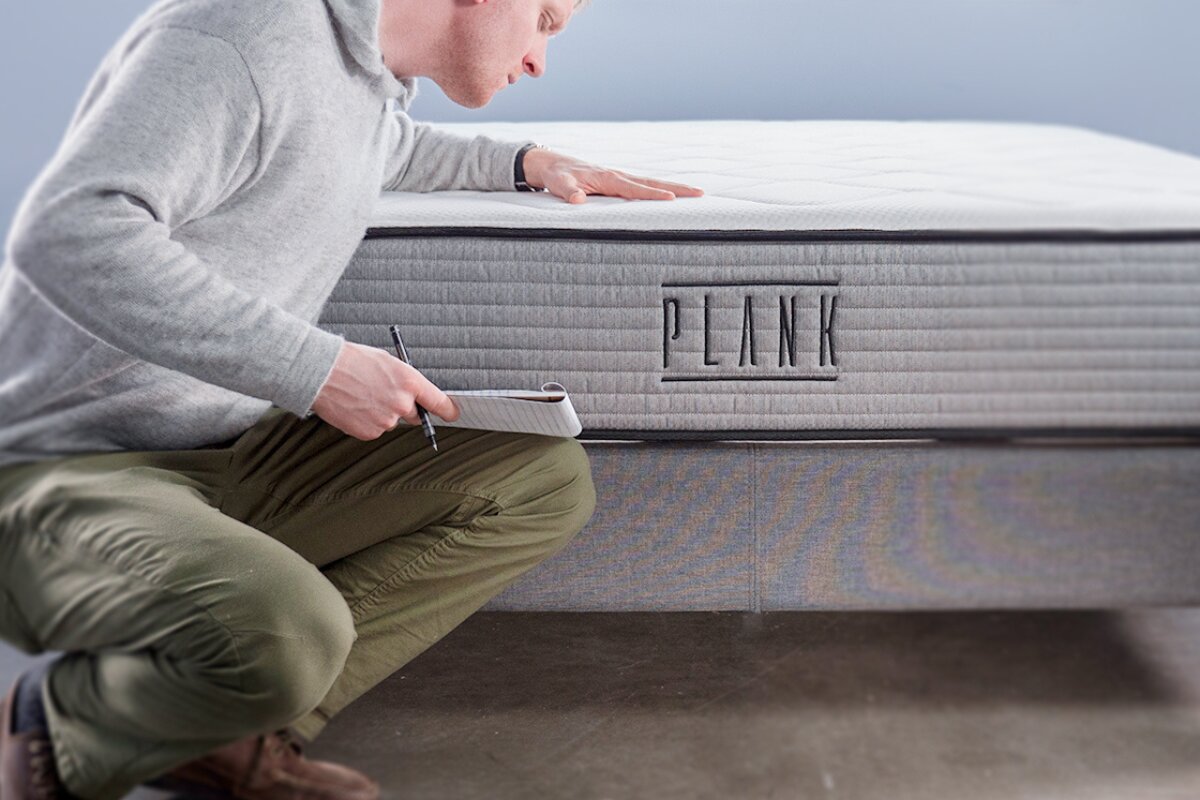 person inspecting a plank mattress and taking notes during a mattress evaluation or warranty assessment