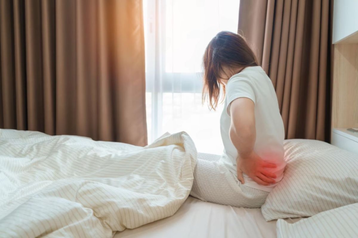 Plush vs Medium Firm Mattress: Which Is Best for Your Sleep? Woman sitting on a mattress with lower back discomfort highlighting how mattress firmness can affect spinal support and sleep comfort