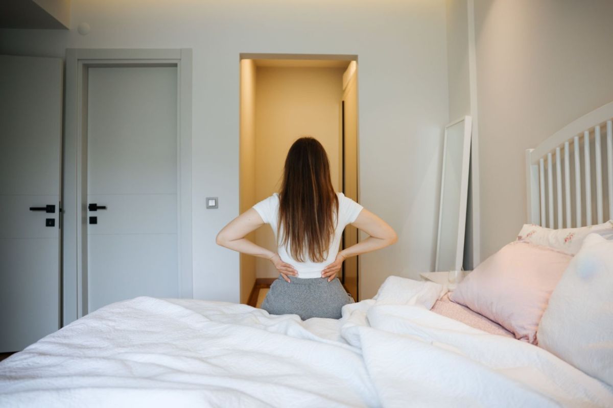 What Does Extra Firm Mattress Mean? Person sitting on bed holding lower back, illustrating discomfort from overly firm mattress support