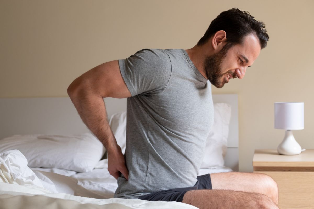 Man sitting on bed with back discomfort showing why some sleepers need a firm mattress