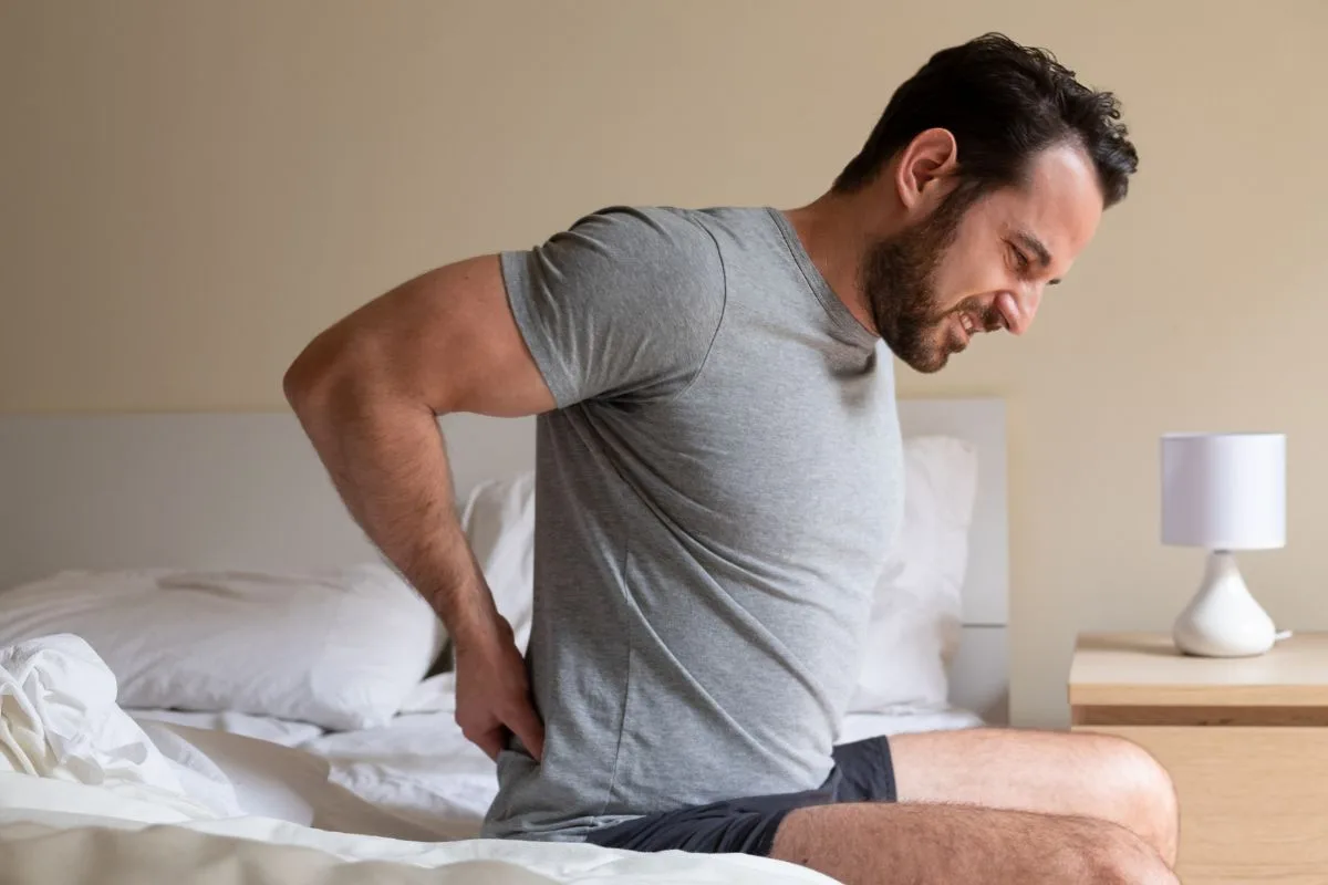 Man sitting on a firm mattress with lower back pain caused by poor pressure relief and support