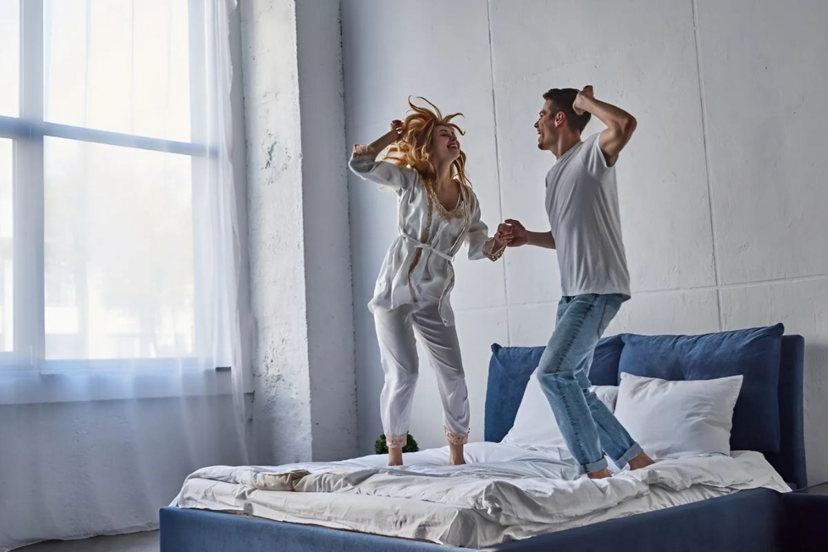 Couple jumping on a bed to show the balanced support and responsiveness of a medium mattress for back comfort