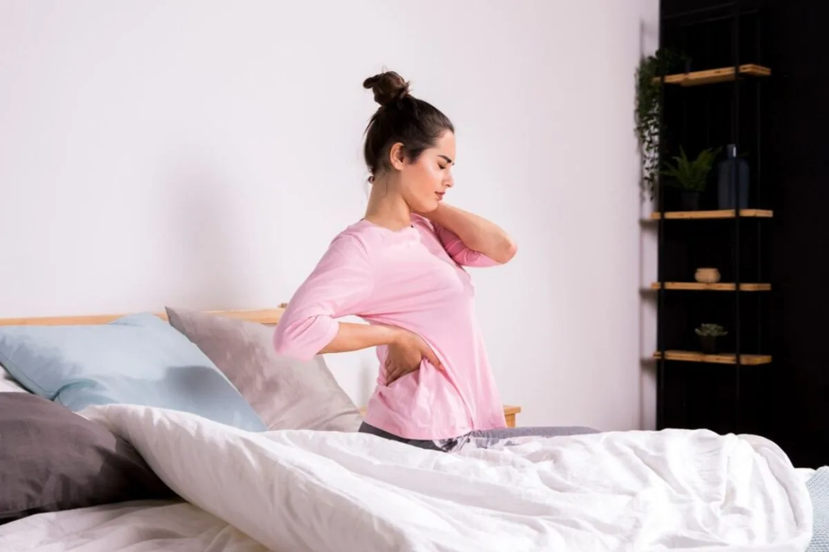 Woman sitting on a bed with lower back pain showing how mattress firmness can affect spinal support and sleep comfort