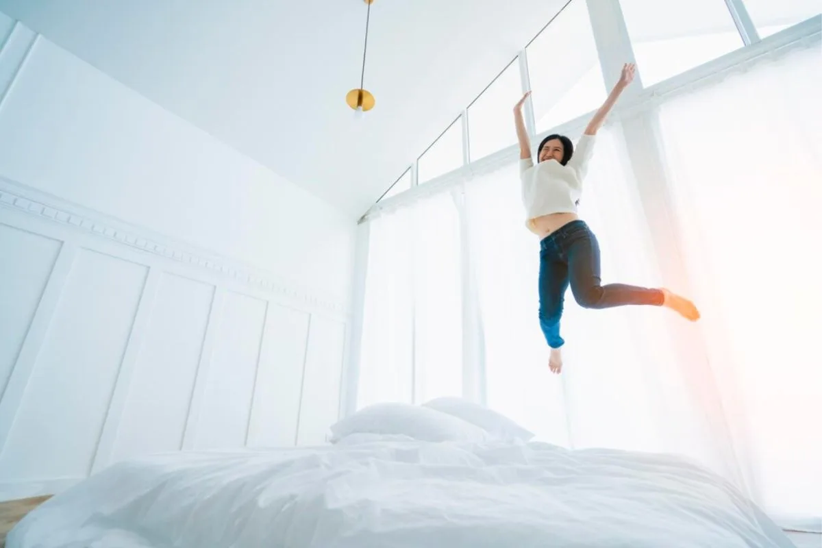 Person happily jumping on a bed showing the cozy and pressure-relieving feel of a medium soft mattress
