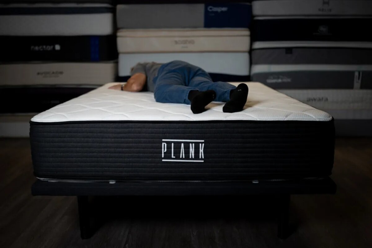 person lying face down on a plank firm luxe mattress in a mattress testing showroom