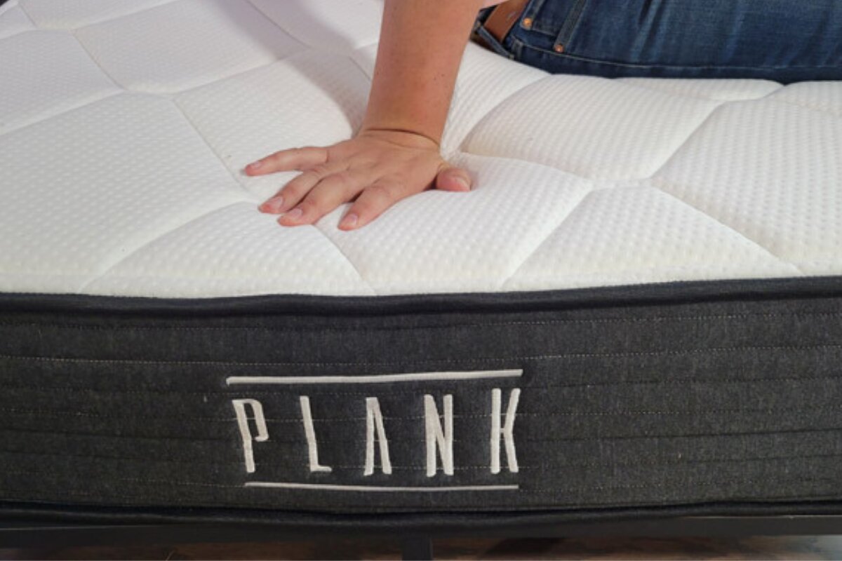 hand pressing into the surface of a plank firm luxe mattress to demonstrate firmness and cushioning response