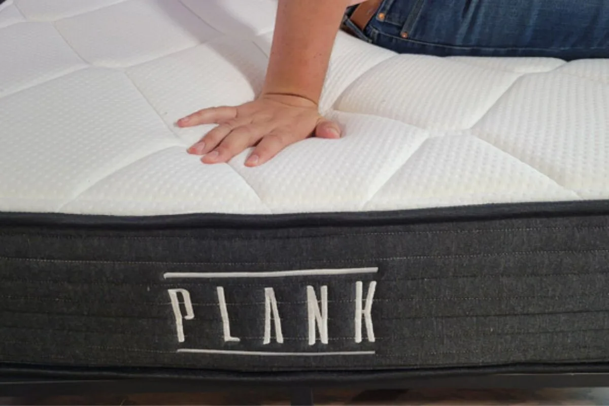 hand pressing into the surface of a plank firm luxe mattress to demonstrate firmness and cushioning response