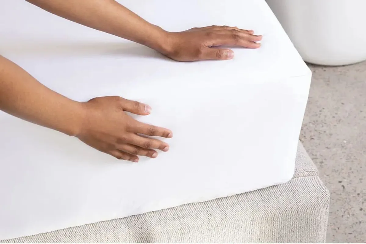 Hands placing a mattress protector on a foam mattress to help prevent stains and protect warranty coverage