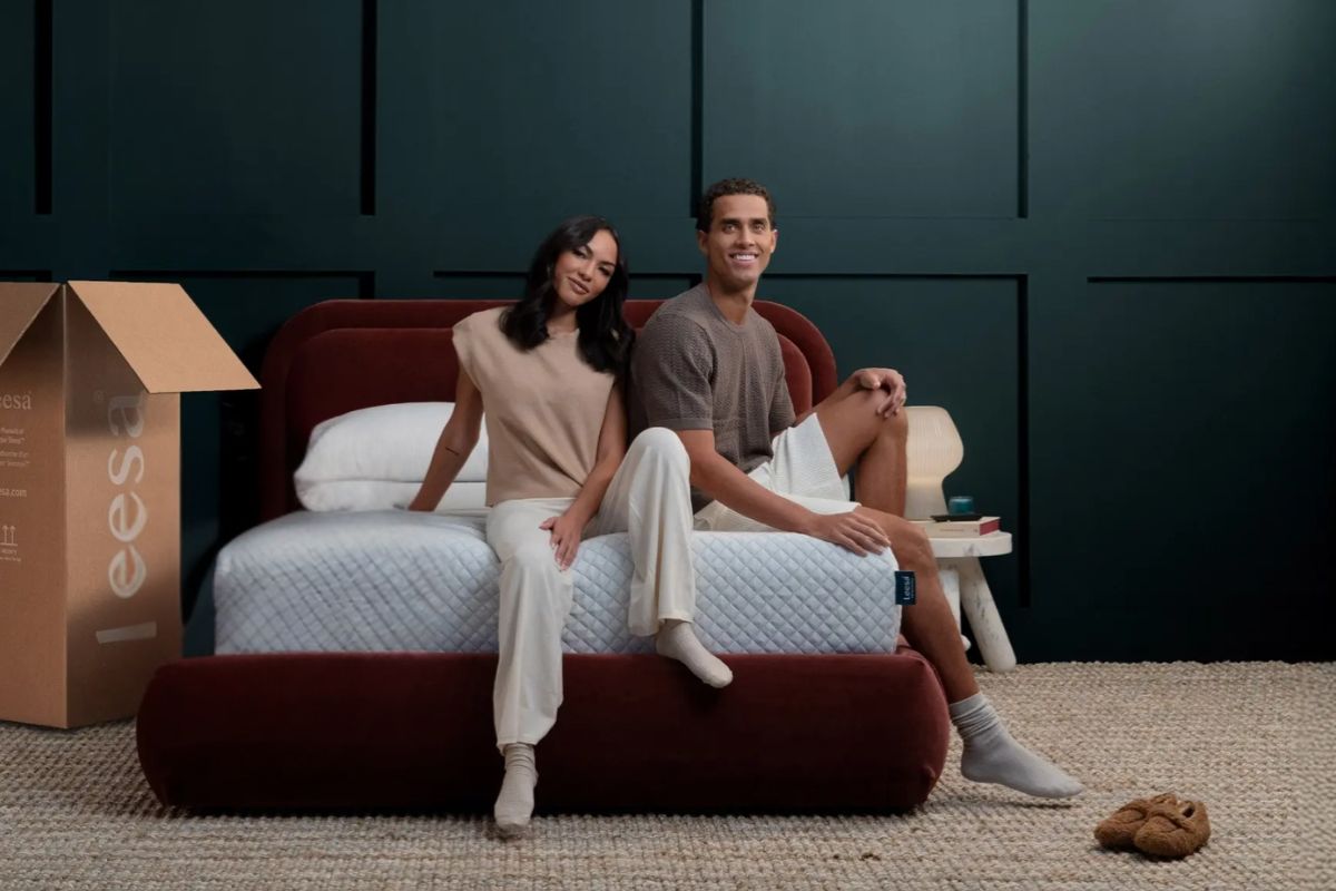 Couple sitting on a Leesa Original Mattress beside the shipping box highlighting proper setup and warranty-safe use