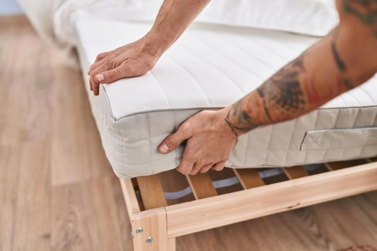 Person turning a hybrid mattress on a wooden bed frame to prevent uneven sagging and wear