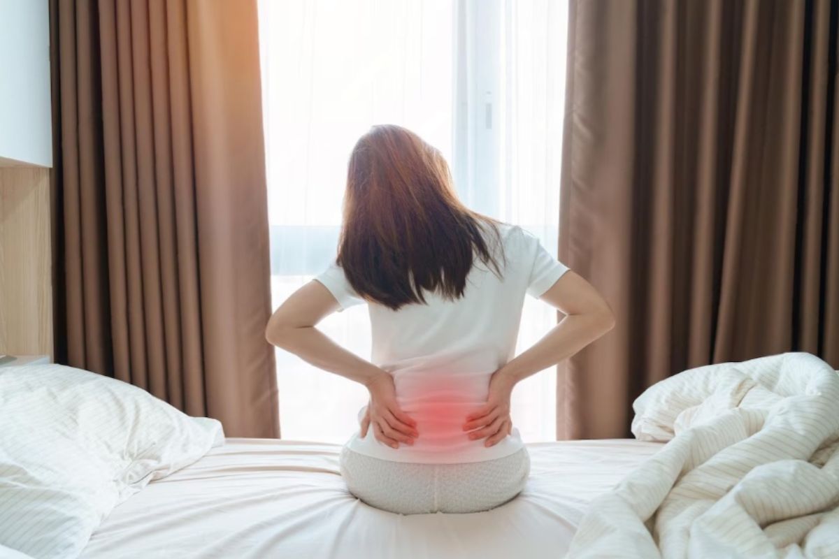 Person experiencing lower back discomfort while sitting on a bed, highlighting a potential sign that an aging innerspring mattress may no longer provide adequate support.