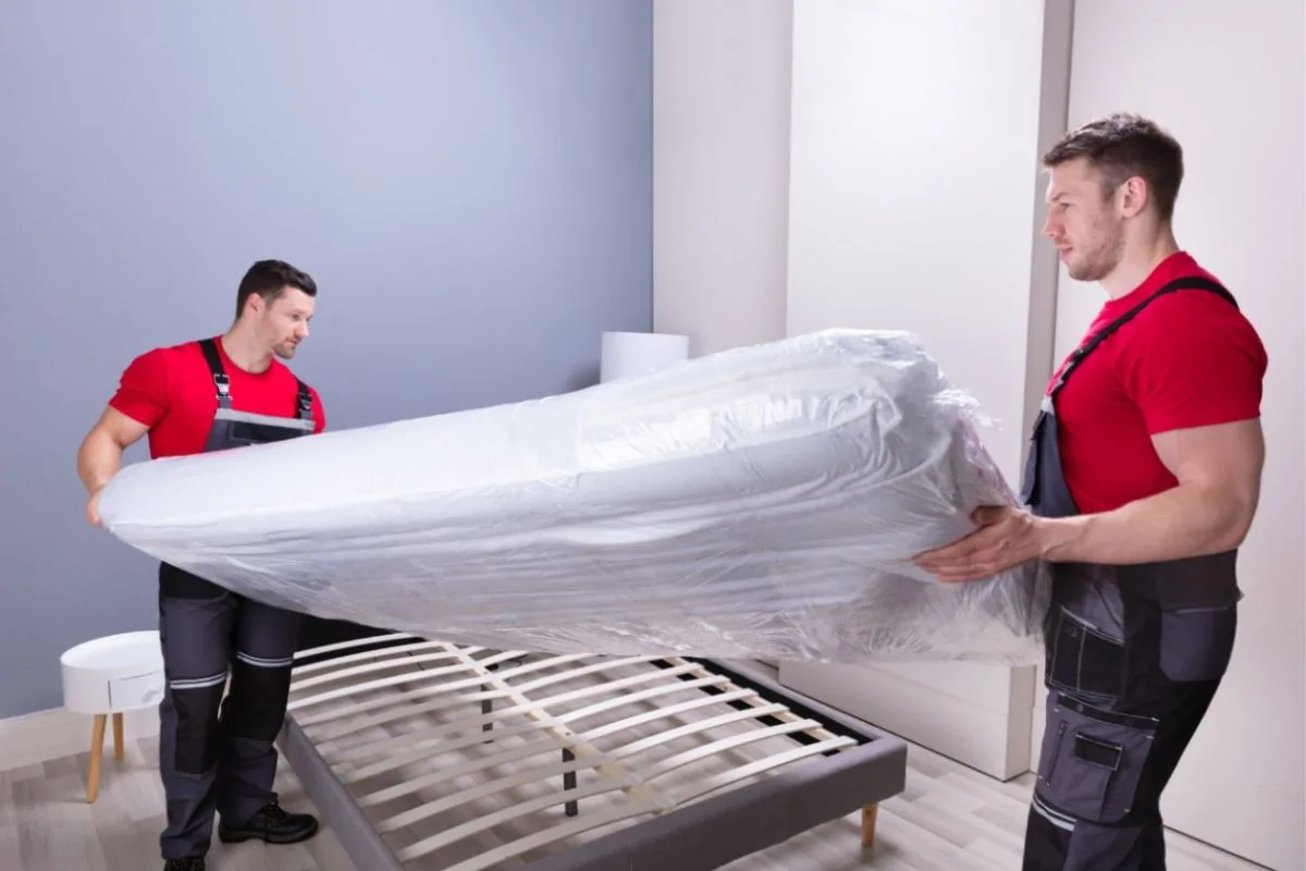 Two movers carrying a hybrid mattress, demonstrating how mattress weight can affect handling, setup, and transportation.