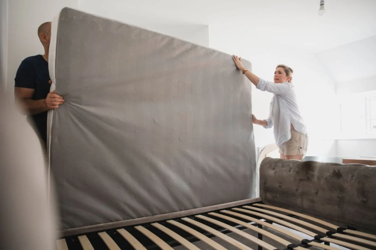 Two people rotating a mattress on a bed frame, demonstrating the proper way to rotate a memory foam mattress for maintenance